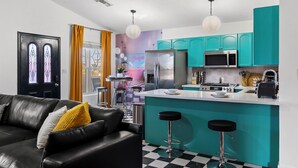 Una cucina moderna con mobili color petrolio, un'isola centrale con sgabelli da bar e un'area pranzo con pavimento a scacchi e un divano in pelle nera.