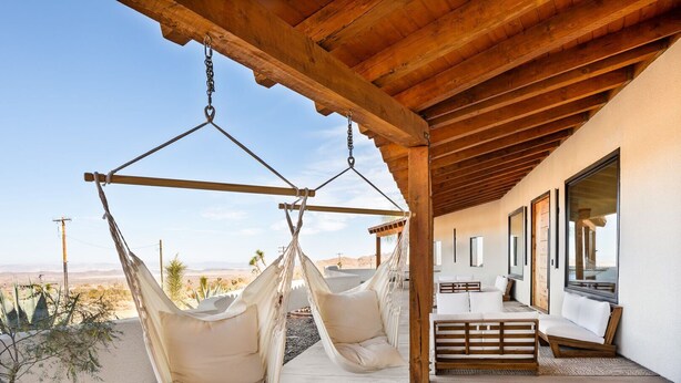 Un moderno espacio lounge al aire libre con dos hamacas colgantes, una terraza de madera y vistas al paisaje desértico.