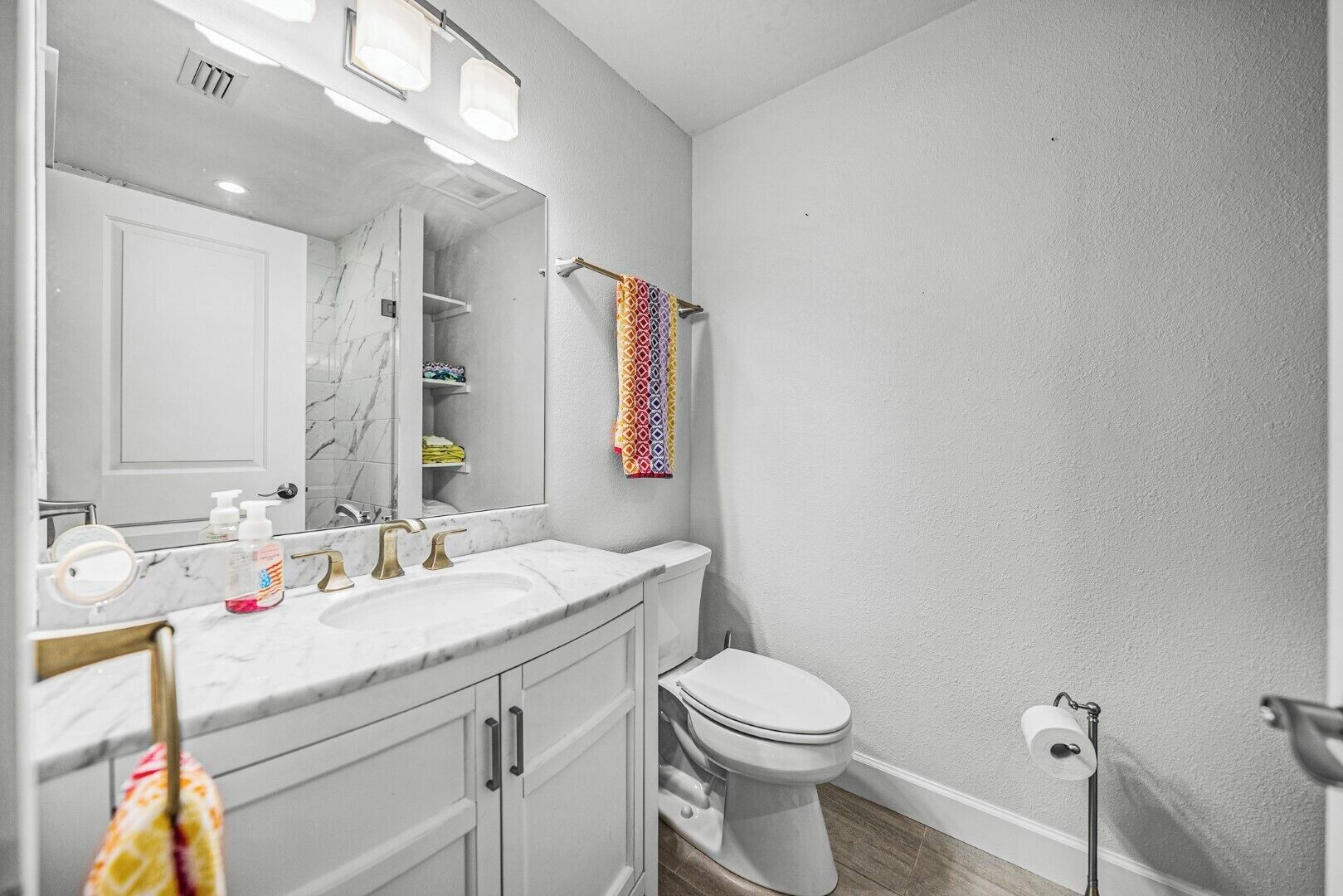 A bathroom with a white marble sink, a toilet, and a towel rack with a colorful towel.