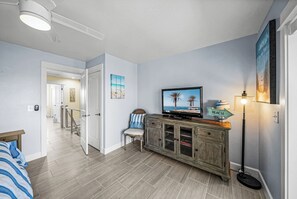 A modern living room with a flat-screen TV, a wooden cabinet, a chair, and a floor lamp. - Gulf Dunes 4 - 2 bed / 2.5 Bath / No Pool / Sleeps 4 - Gulf Front (Boca Grande)