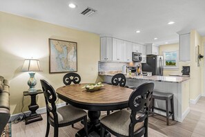A modern kitchen with white cabinets, a central island, and a dining area with a round table and chairs. - Gulf Dunes 4 - 2 bed / 2.5 Bath / No Pool / Sleeps 4 - Gulf Front (Boca Grande)