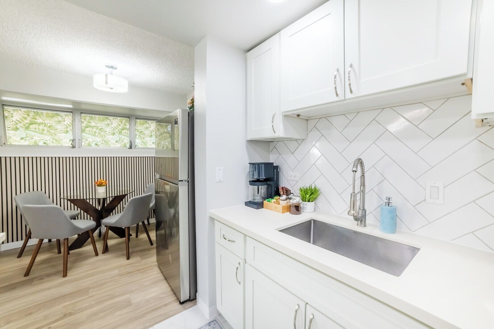 A modern kitchen with white cabinetry, a stainless steel sink, and a dining area with a round table and chairs.