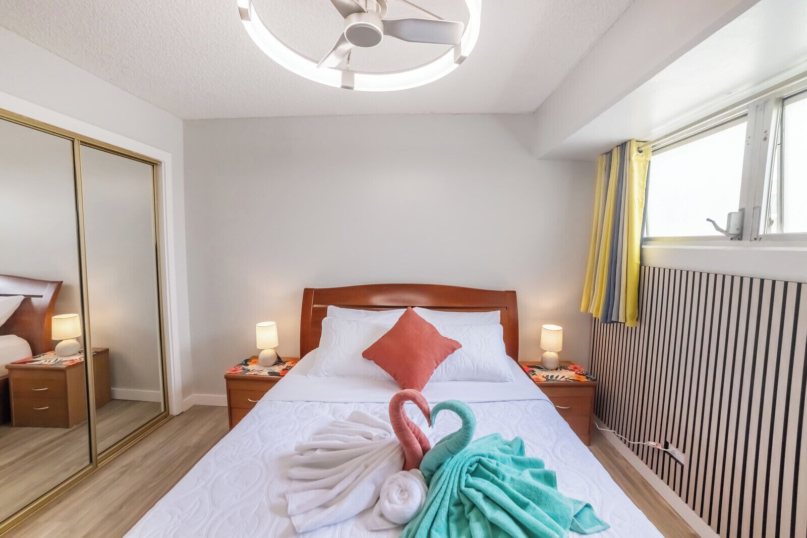 Ein Hotelzimmer mit einem Bett, zwei Nachttischen mit Lampen, einem Spiegel, einem Heizkörper und einem Fenster mit Vorhängen.