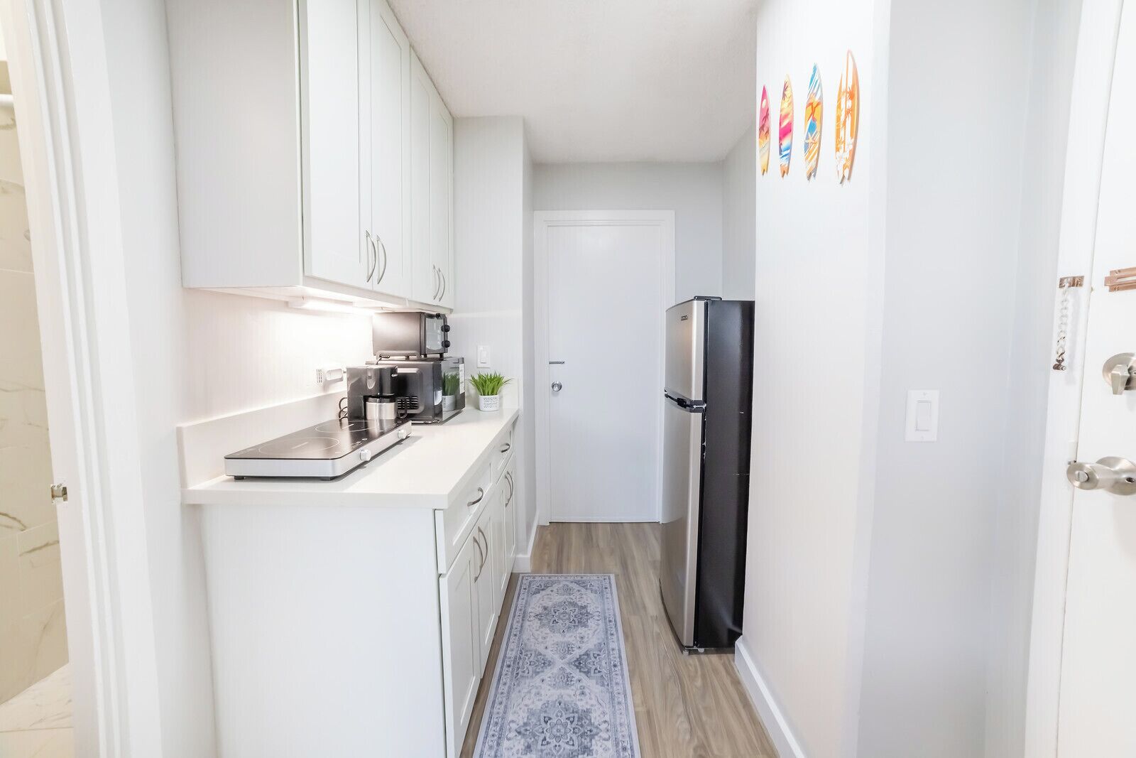 A compact kitchen with white cabinets, a black refrigerator, a coffee maker, and a small plant.
