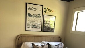 A bedroom with a wooden headboard, a bed with multiple pillows, a framed picture of Lake Tahoe, and a sign for the Campfire Club. - Lovely updated  3-bedroom condo on the Lake (Incline Village)