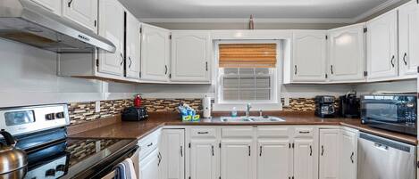 Una cocina moderna con armarios blancos, electrodomésticos de acero inoxidable y una ventana con persianas.