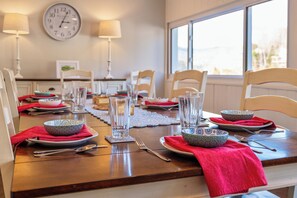 Une table à manger dressée avec des bols, des verres et des couverts, une horloge au mur et une fenêtre en arrière-plan.