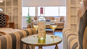 Una bottiglia di vino La Gala su un tavolo con due bicchieri di vino bianco, in un soggiorno con divani a righe e una libreria sullo sfondo.