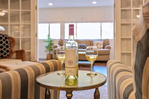 Eine Flasche La Gala Wein auf einem Tisch mit zwei Weingläsern, in einem Wohnzimmer mit gestreiften Sofas und einem Bücherregal im Hintergrund.