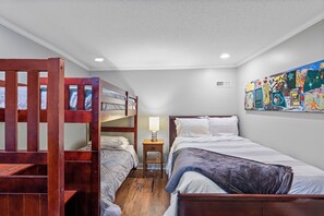 Une chambre de dortoir avec des lits superposés, un lit simple, une table de chevet avec une lampe et une œuvre d’art colorée accrochée au mur.