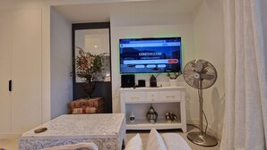 A modern living room with a flat-screen TV, a white console table, a floor fan, and decorative items. - dream studio getaway (Gibraltar)