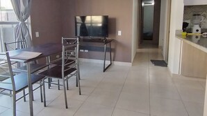 Un soggiorno moderno con una televisione a schermo piatto, un tavolo da pranzo con sedie e una zona cucina con un piano di lavoro ed elettrodomestici.