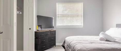 A bedroom with a bed, a dresser, a television, and a window with blinds.