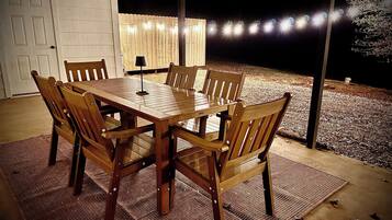 Een buiten eethoek met een houten tafel en stoelen, een vloerkleed en sfeerverlichting.