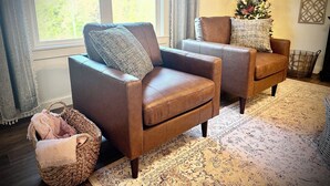 A living room with two brown leather armchairs, a woven basket, a Christmas tree, and a patterned rug.