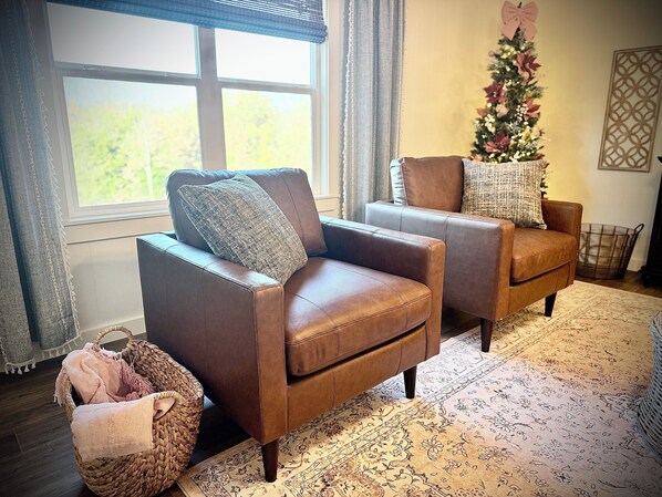 A living room with two brown leather armchairs, a woven basket, a Christmas tree, and a patterned rug.
