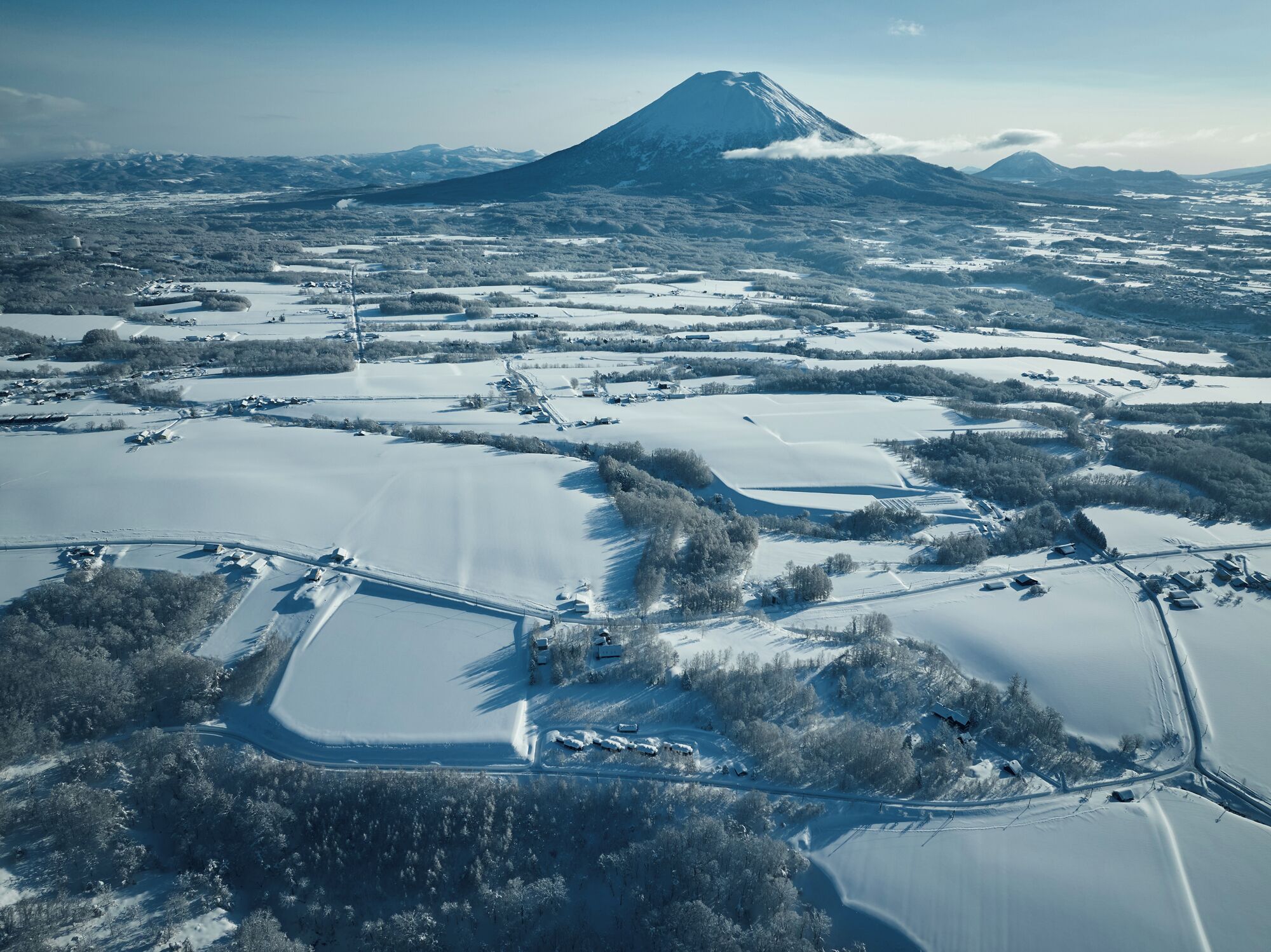 Eine Luftaufnahme einer verschneiten Landschaft, im Hintergrund ein markantes Gebirge.