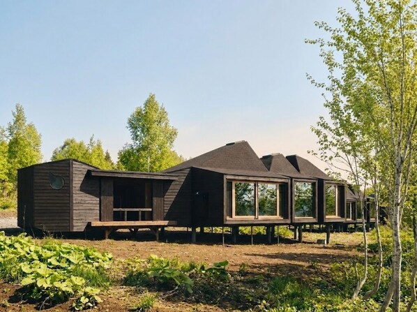 A modern, wooden cabin with large windows and a sloped roof, situated in a natural setting with trees and greenery. - SANU 2nd Home Niseko 1st (Niseko)