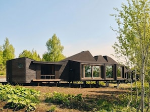 A modern, wooden cabin with large windows and a sloped roof, situated in a natural setting with trees and greenery.