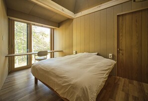 A bedroom with a large bed, wooden walls, a window with a view of trees, and a wooden door. - SANU 2nd Home Niseko 1st (Niseko)