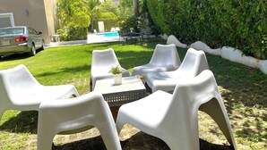 Une terrasse avec des chaises et une table en plastique blanc, une piscine et un bâtiment en arrière-plan.