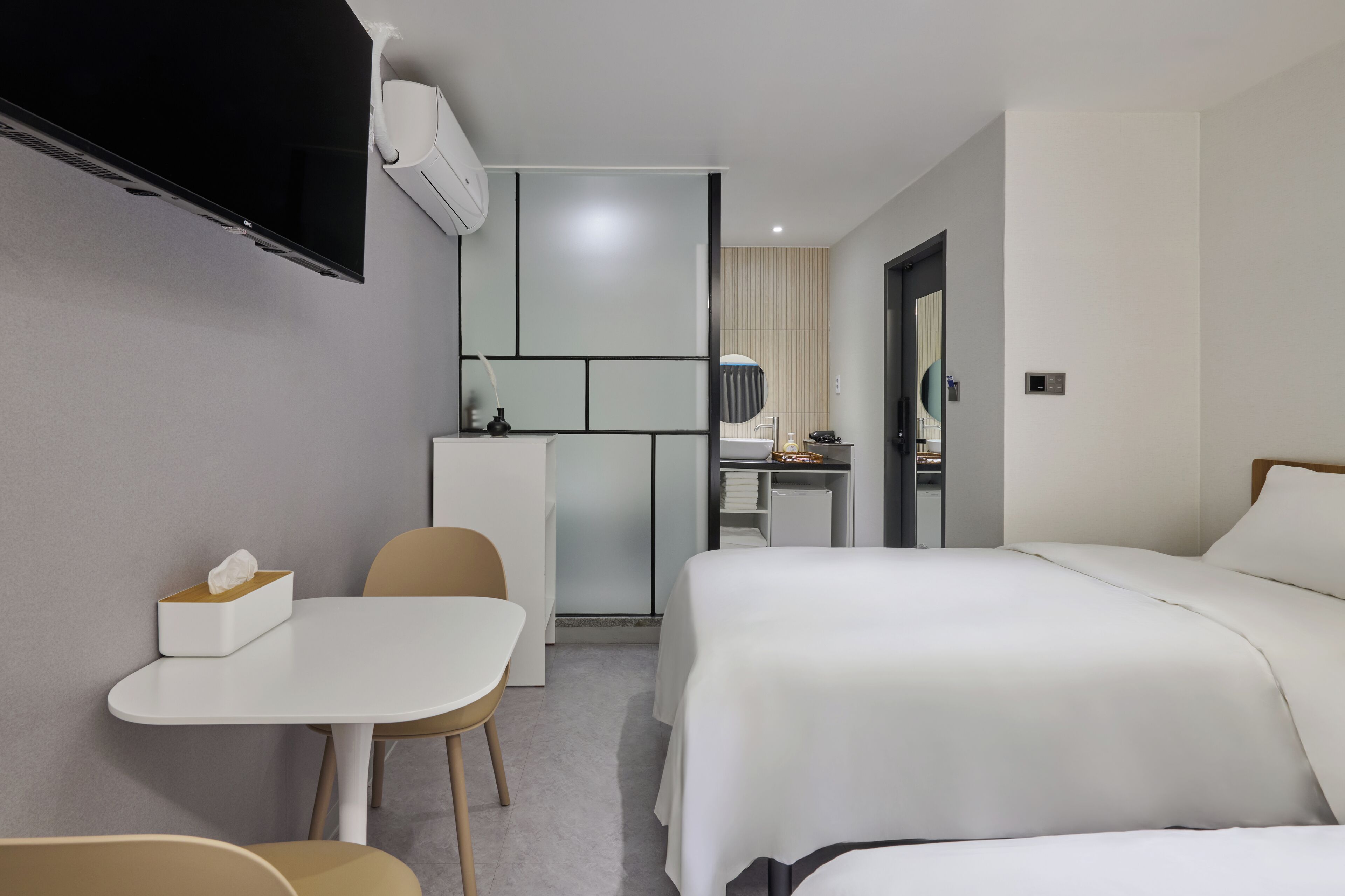 Quarto de hotel com cama, escrivaninha, cadeira, televisão e uma pequena cozinha equipada.