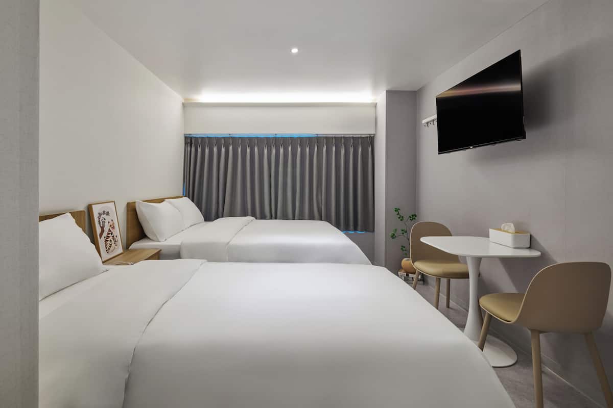 Habitación de hotel con dos camas, un televisor de pantalla plana, una mesita con sillas y una ventana con cortinas.