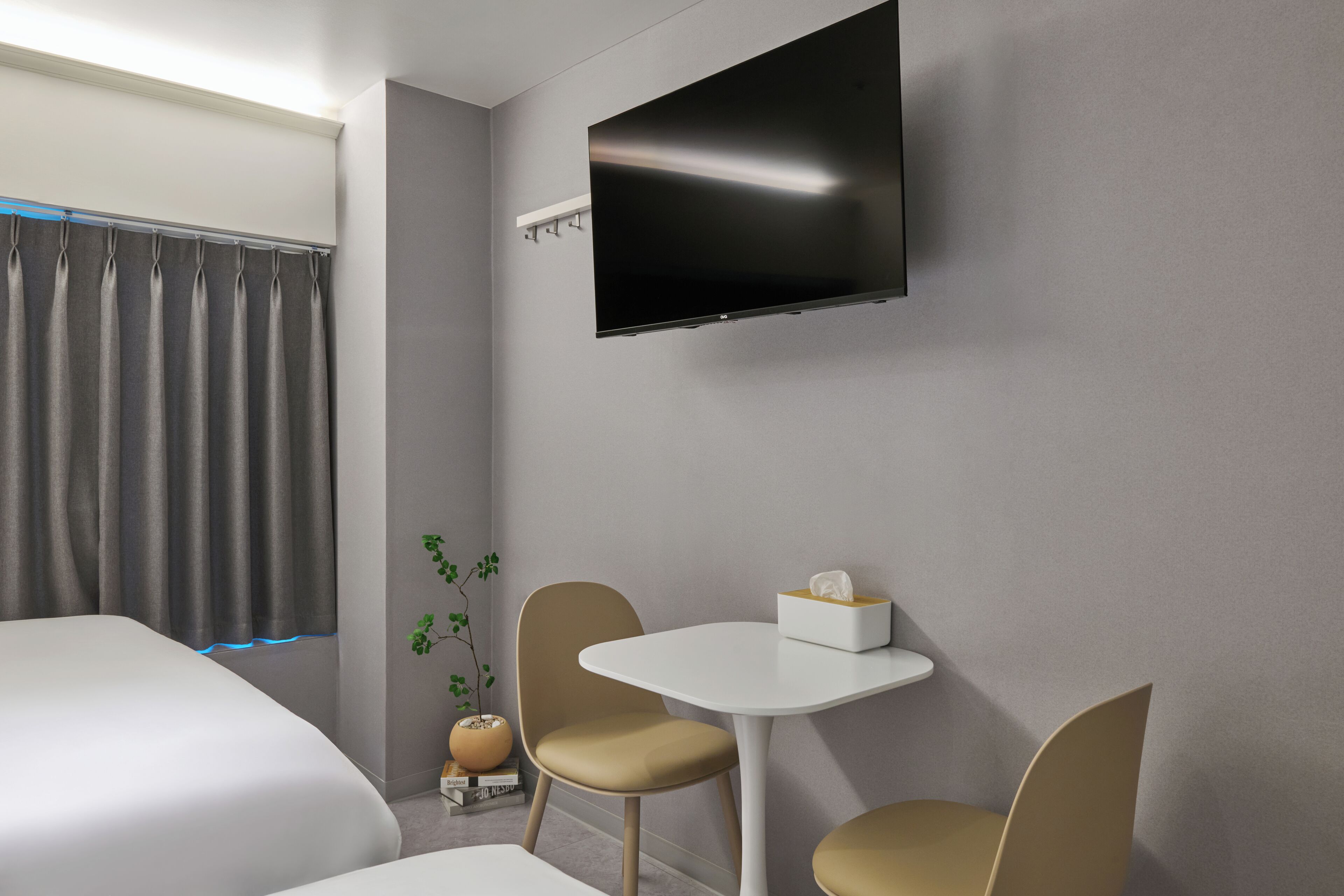 Una habitación de hotel moderna con una cama, una mesita con sillas, un televisor de pantalla plana en la pared y una ventana con cortinas.