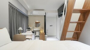 A modern hotel room with a bed, a desk with a chair, a vanity with a mirror, a wooden ladder, and an air conditioning unit. - N Joy Stay (Seoul)