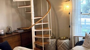 Eine Wendeltreppe mit Holzvertäfelung, ein Sofa mit gemusterten Kissen und ein Fenster mit Vorhängen.
