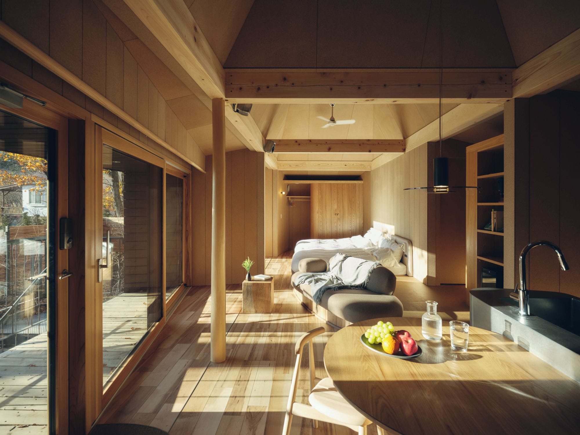 A modern interior with a wooden floor, a dining area with a fruit bowl, a sofa, and a kitchen area with a sink.