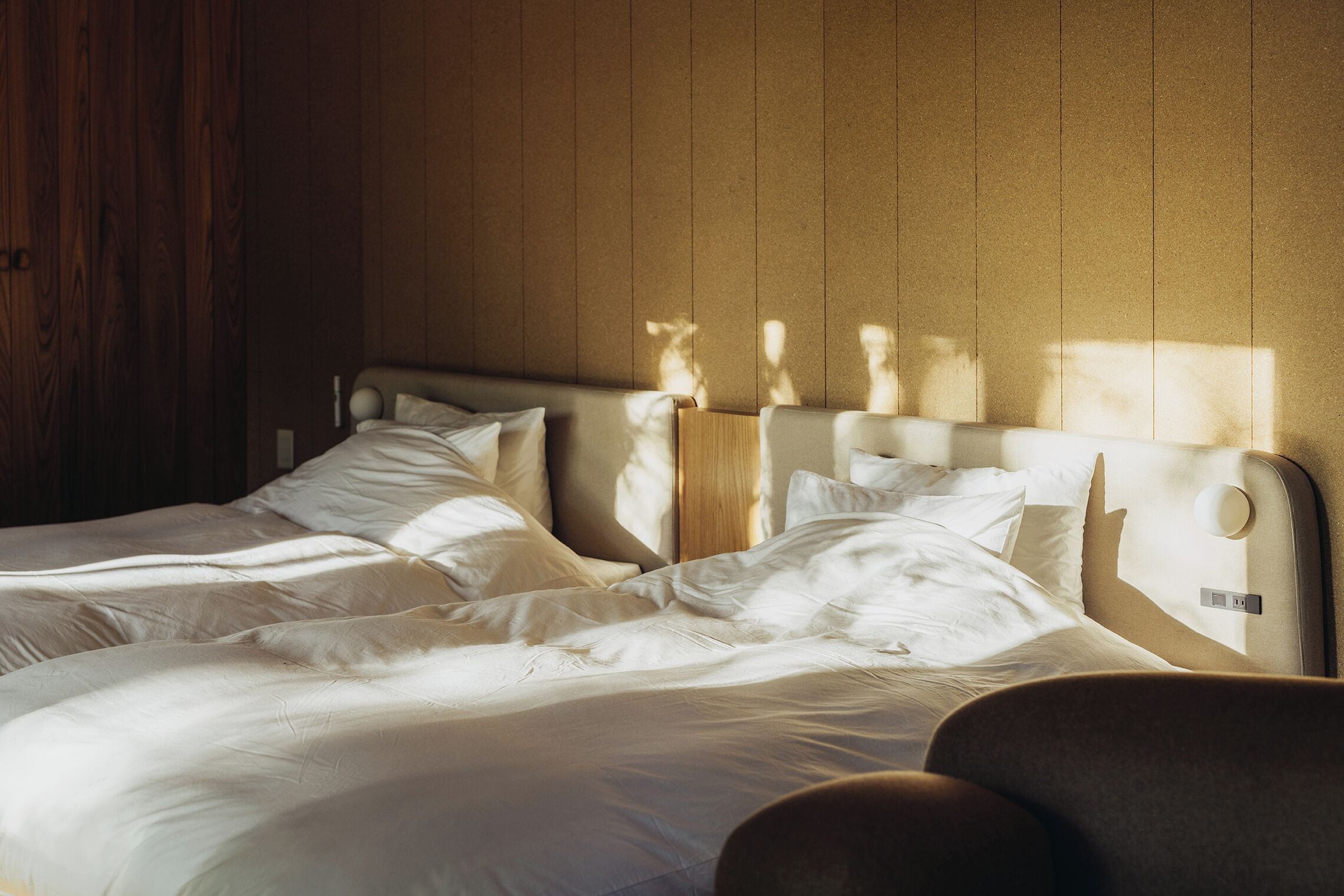 A double bed with white linens in a room with wooden panel walls.