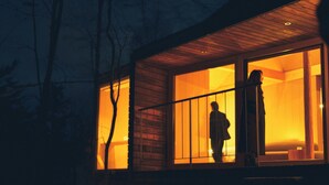 Un edificio moderno con amplios ventanales, revestimiento de madera y un interior visible donde se ve a una persona de pie.
