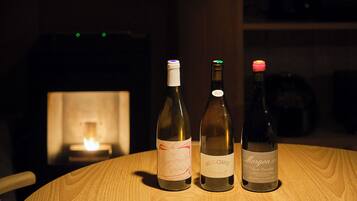 Three wine bottles on a round wooden table with a lit fireplace in the background.