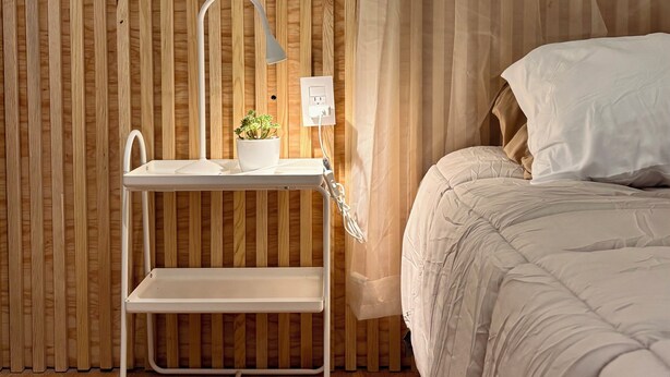A neatly organized bedroom with a wooden slat wall, a bedside table with a lamp, a power outlet, and a potted plant. - "Casa del sol" ideal for families, well located, comfortable, equipped and safe. (Santiago de Querétaro)