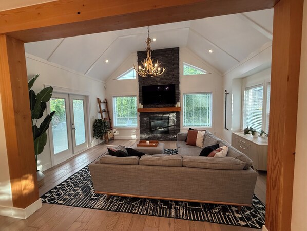 A spacious living room with a fireplace, a large sofa, and a chandelier. - Luxury Mountain Retreat in Squamish (Squamish)