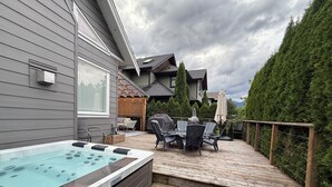 Een terras met een jacuzzi, buitenmeubels en uitzicht op een huis.