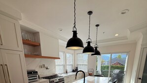 Een moderne keuken met een groot eiland, witte kasten en zwarte hanglampen.