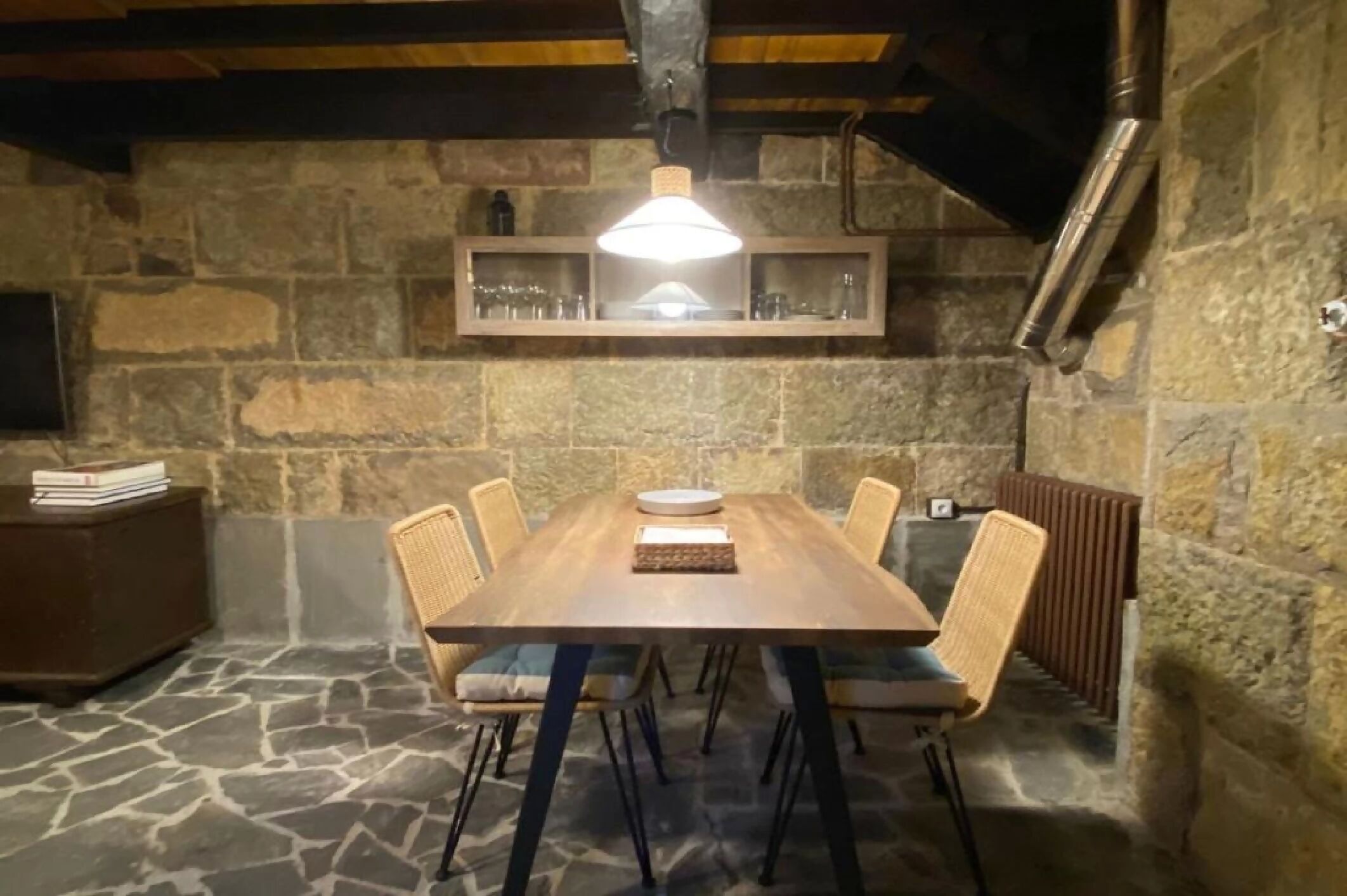 A stone-walled dining area with a wooden table, wicker chairs, and a hanging light fixture.