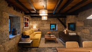 Una habitación acogedora con paredes de piedra, un sofá amarillo, una mesa de centro de madera, sillones de mimbre, un televisor y una chimenea.