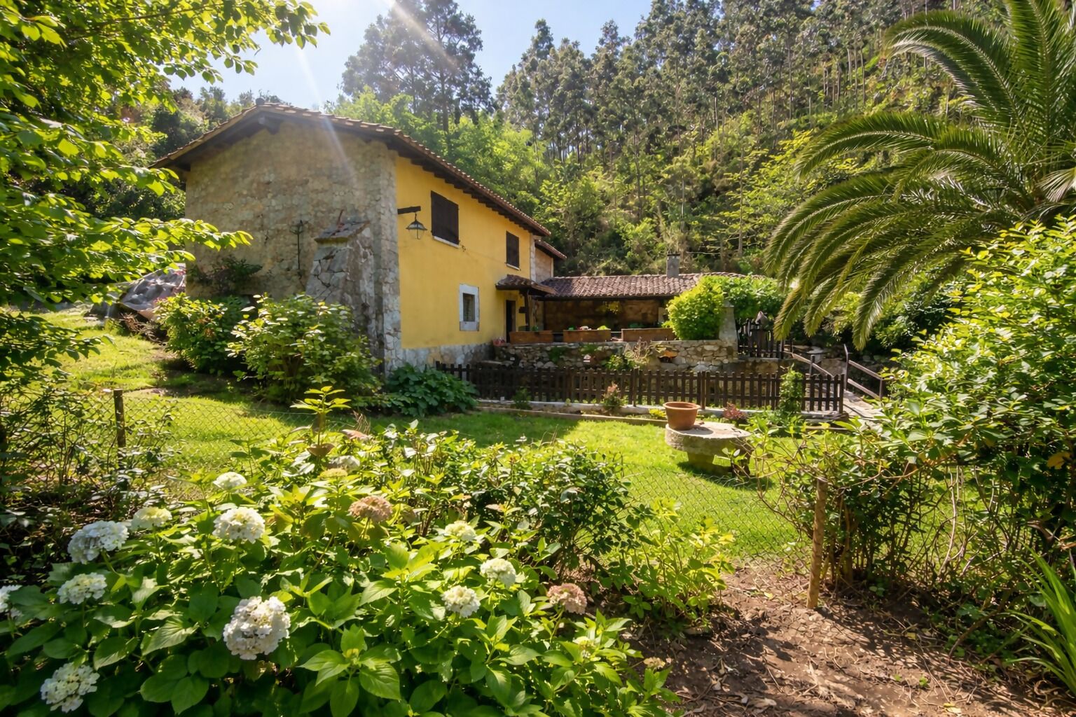 Een geel huis met een stenen gevel, omgeven door weelderig groen en een verzorgde tuin.