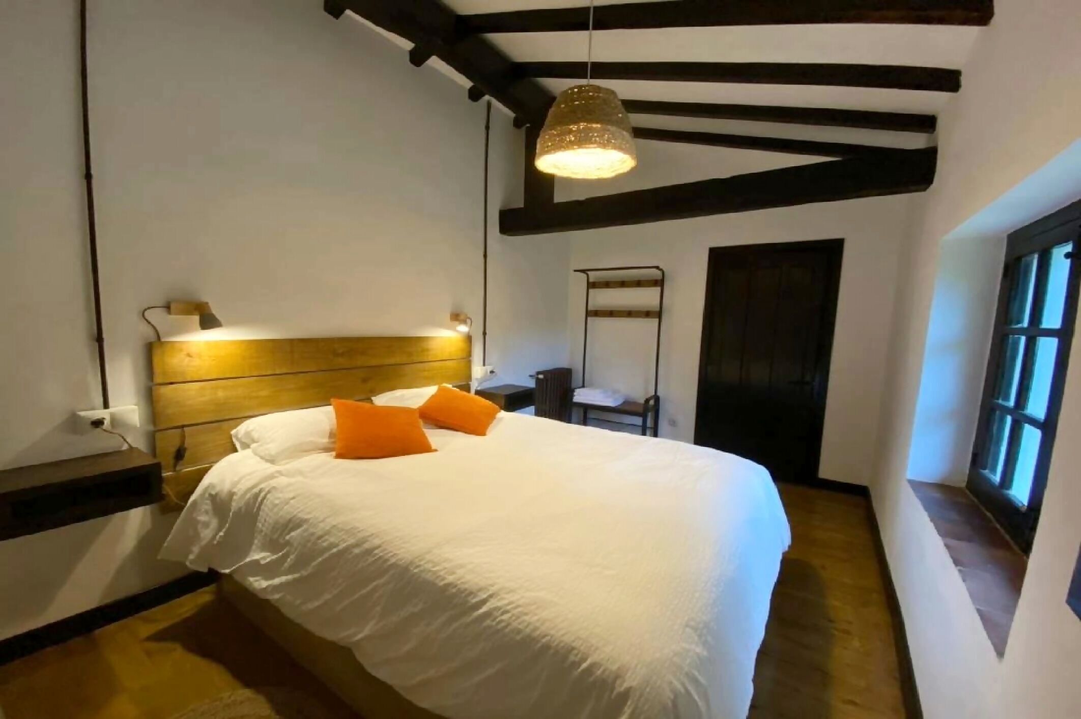 Une chambre à coucher avec un lit, une table de chevet, un luminaire suspendu et une fenêtre.