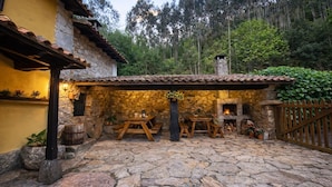 Un patio rústico al aire libre con paredes de piedra, mesas de madera y una chimenea de piedra.