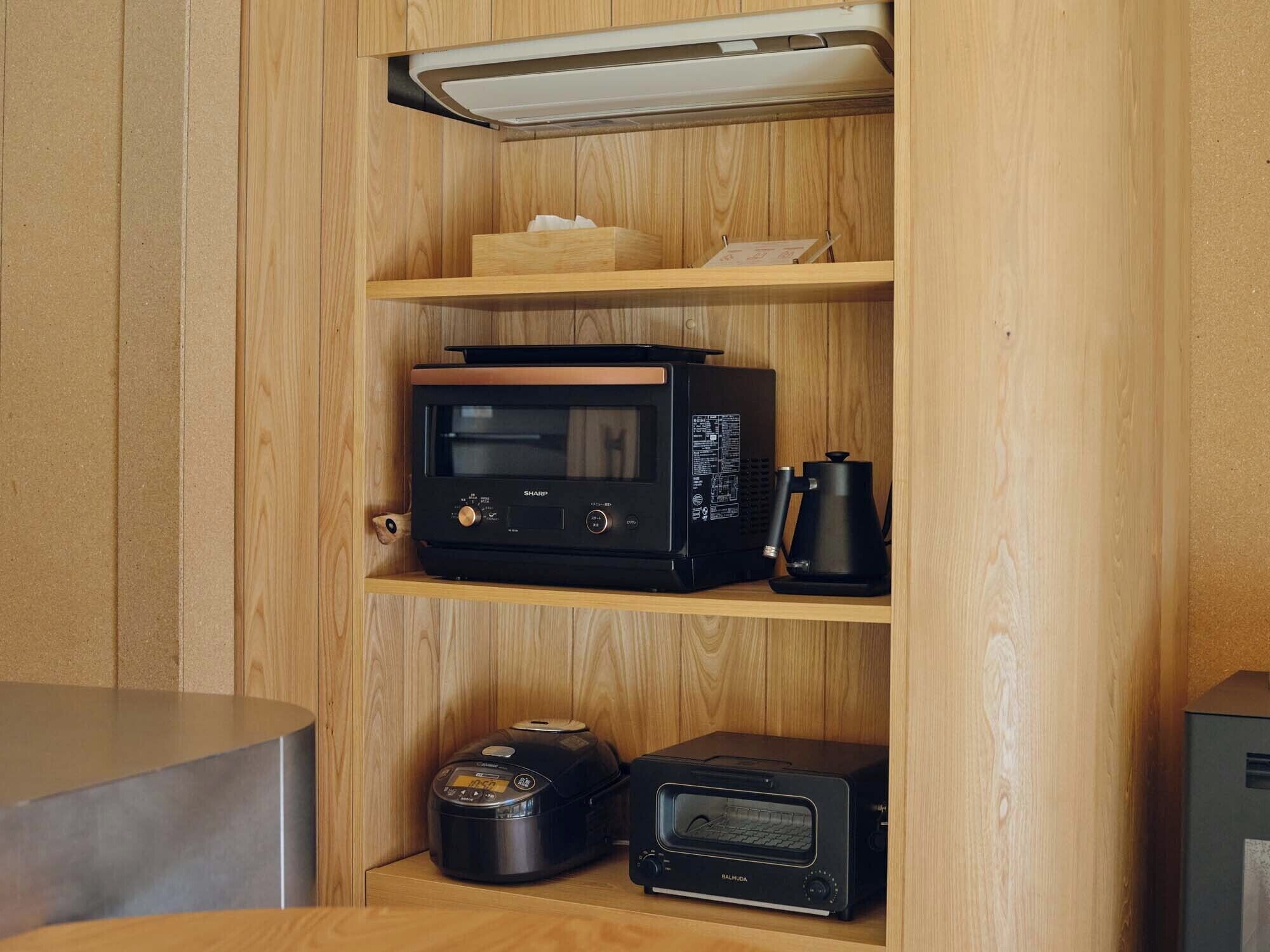 A compact kitchen with a microwave, toaster, and coffee maker on wooden shelves.