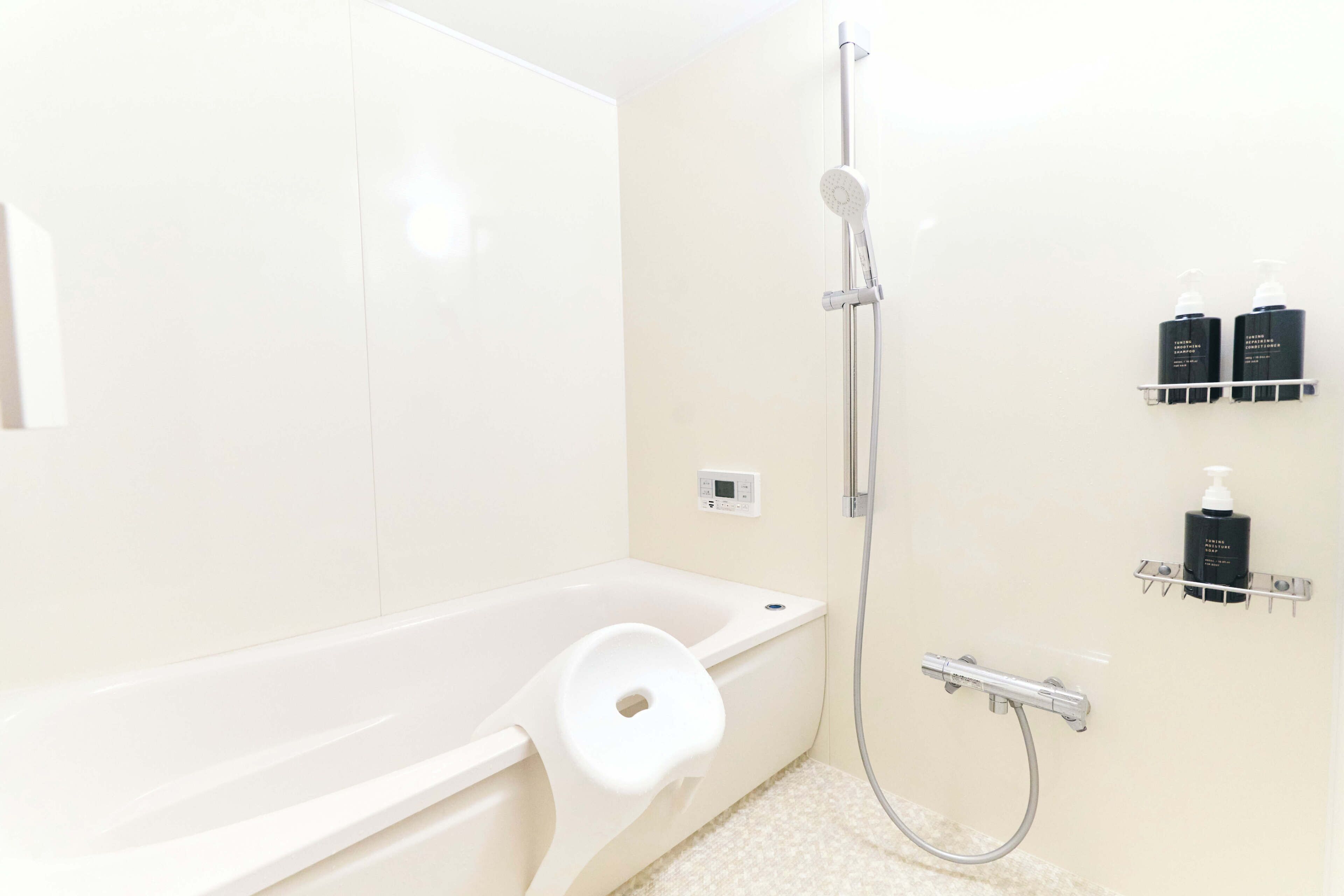 A modern bathroom with a white bathtub, a handheld showerhead, and two black toiletry bottles on a wall-mounted shelf.