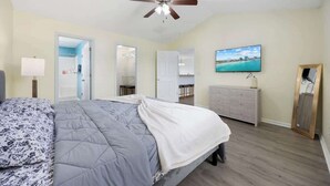 Un dormitorio con cama, ventilador de techo, televisor, cómoda y espejo.