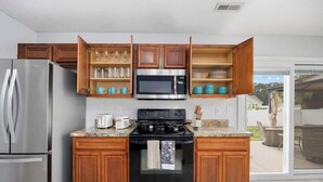 Una cocina con un refrigerador de acero inoxidable, un microondas, una estufa, armarios de madera y una puerta corrediza de vidrio al exterior.