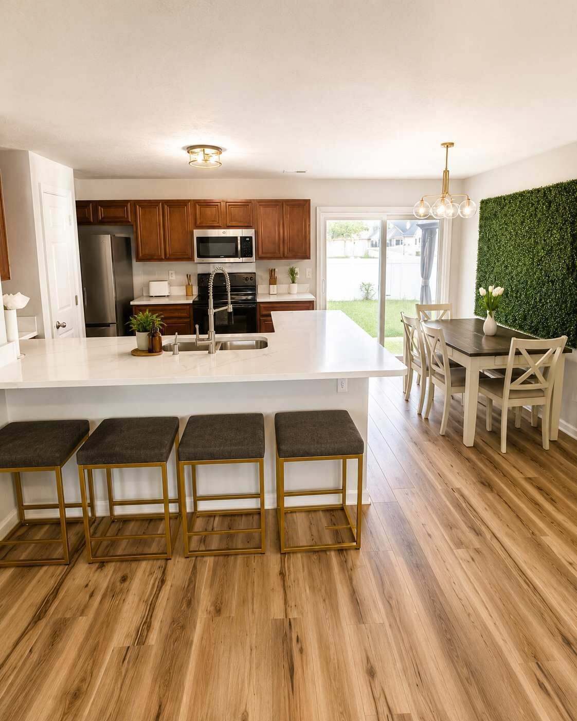A modern kitchen with a central island, wooden cabinets, and a dining area with a green wall and natural light.