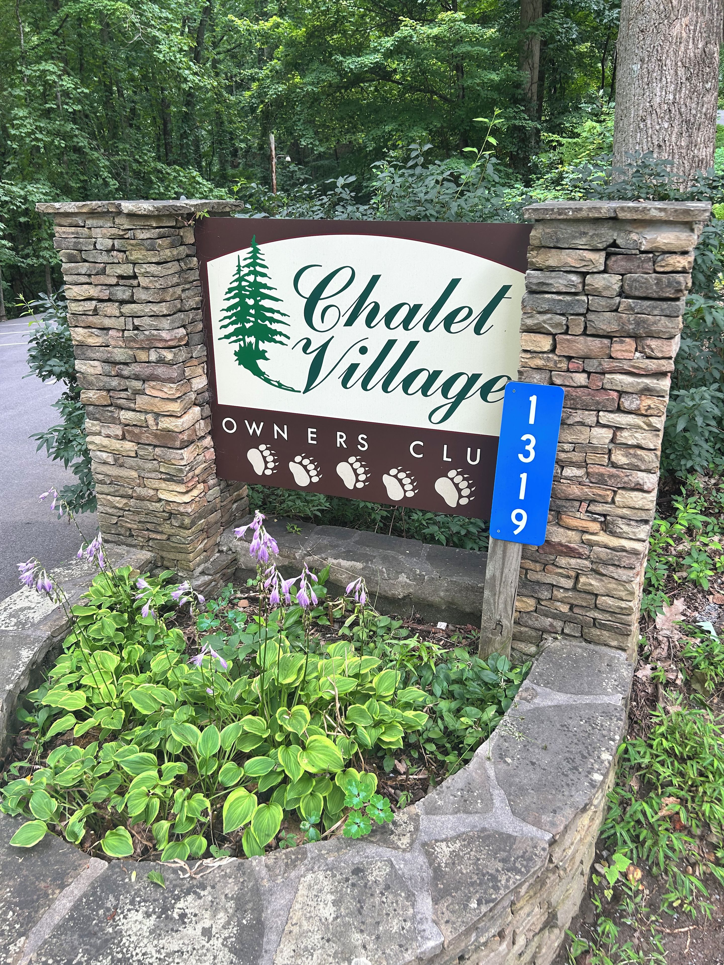 A sign for Chalel Village Owners Club with a stone wall and a blue house number sign.
