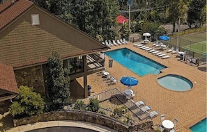 Uma área de piscina com espreguiçadeiras e guarda-sóis, uma piscina pequena e circular, e um edifício com fachada de pedra.